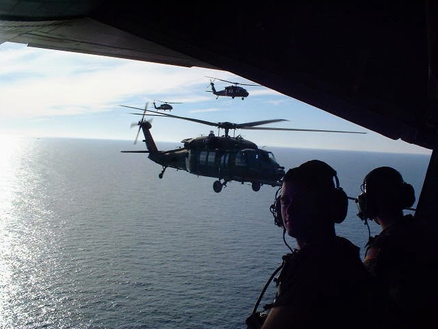 Helicopters flying in formation over the ocean, seen from the open troop door past two crew members in headsets, 2002.