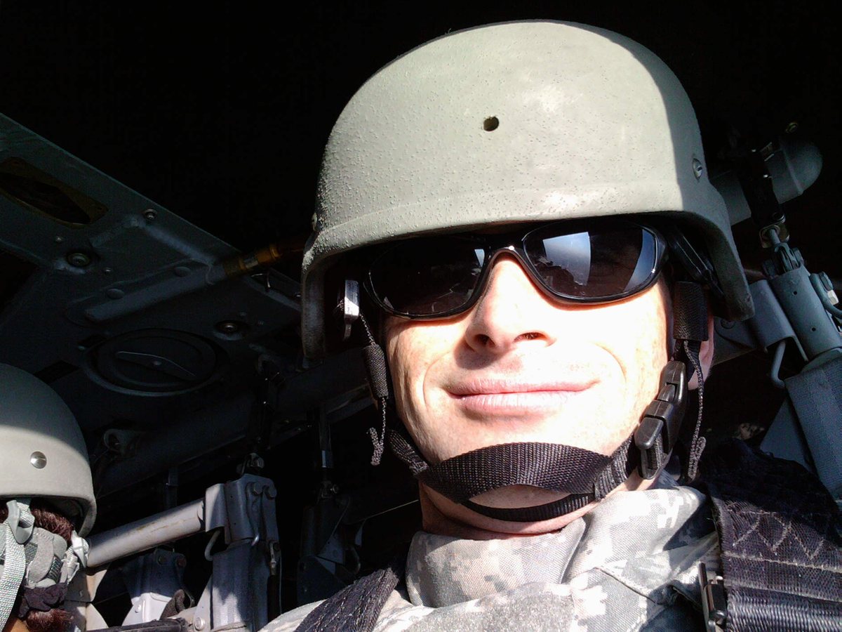 Ken in a helmet, sunglasses, and body armor, smiling inside a military aircraft in 2011.